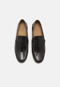 Mocassins en cuir verni noir avec un bout arrondi, ornés de coutures décoratives et d'une lanière en penny sur le devant. Fini lisse et brillant.
