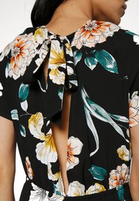 Black floral dress with short sleeves, featuring a back cutout and tie closure. The fabric displays large, colorful floral patterns.