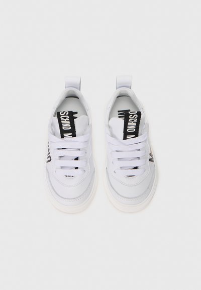 Valge madala profiiliga sneakers paar, valgete paeltega ja mustade bränditud tõmblukkudega keeles, vaadatud pealt valgel taustal.