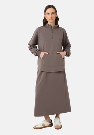 Felpa leggera di colore malva con mezza zip, maniche lunghe, tasca frontale, abbinata a una gonna maxi coordinata e sneaker casual.