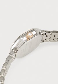 Montre en acier inoxydable argenté avec une finition polie, un cadran rectangulaire, une couronne dorée et un bracelet de type bande.