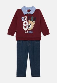 Sweat-shirt bordeaux avec un graphisme d'ours et du texte, associé à un pantalon en denim bleu. Le sweat-shirt possède un col bleu clair.