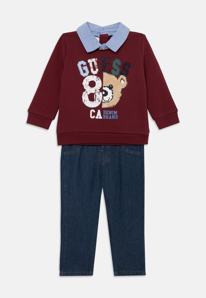 Felpa bordeaux con grafica di un orso e testo, abbinata a pantaloni di jeans blu. La felpa presenta un colletto blu chiaro.