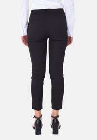 Pantaloni neri aderenti con una texture liscia, lunghezza alla caviglia e due tasche posteriori. Abbinati a scarpe nere con tacco a blocco.