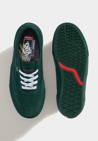 Zapatillas de ante verdes con cordones blancos, que cuentan con una plantilla acolchada y una suela de goma texturizada. Acento rojo notable en la suela.
