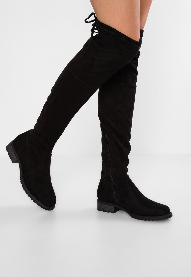 Botas de gamuza negras por encima de la rodilla con suela plana, cremallera lateral y cordones ajustables en la parte superior, con un acabado suave y texturizado.