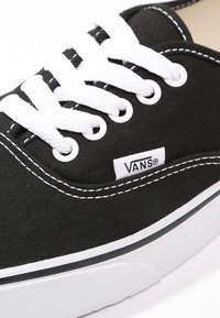Black canvas sneaker with white laces, featuring a white Vans logo tag, clean stitching, and a rubber sole with a black stripe accent.