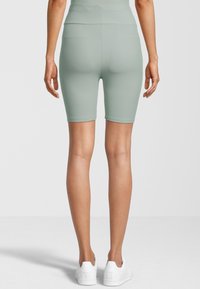 Shorts da bici a coste verde menta con vita alta. Il tessuto ha una consistenza liscia e si estende fino a metà coscia. Viene indossato un paio di sneakers bianche.