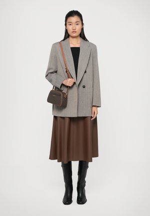 Blazer grigio a doppio petto, top nero, gonna midi marrone e stivali neri al ginocchio. Borsa marrone con motivo decorativo e tracolla.