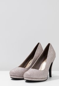 Tacones brillantes color rosa dorado con punta redondeada, suela de plataforma y un tacón delgado negro, con un forro interior suave.