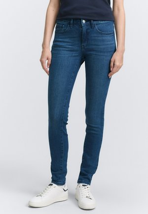 Skinny-fit blue jeans made of denim with a smooth texture, featuring a front button closure and side pockets, paired with white sneakers.