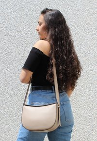 Beige læder crossbody taske med en buet form, tekstureret overflade og en kontrasterende mørk kant. Justerbar rem for alsidig bæring.