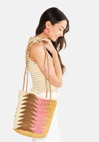 Kudottu olkalaukku, jossa on sahalaitakuviot ruskeassa, vaaleanpunaisessa ja kermassa. Varustettu punotuilla kahvoilla ja tilavalla muotoilulla, jota korostaa hillitty brändäys.