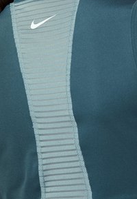 Gros plan d’un tissu sportif turquoise avec un panneau central côtelé et un logo Nike blanc en haut à gauche.