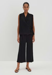 Black wrap top with a tie detail, paired with wide-leg black trousers. Smooth fabric with a matte finish. Simple, minimal design.