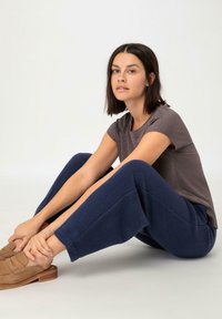 Grijze T-shirt met korte mouwen gecombineerd met marineblauwe fleece joggingsbroek. Model poseert op de grond en draagt bruine instappers. Zachte, casual stoftexturen.