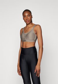 Under Armour sports-bh i taupe med grå detaljer, med justerbare stropper og et stilrent, stretchy design. Kombinert med svarte høyt liv leggings.
