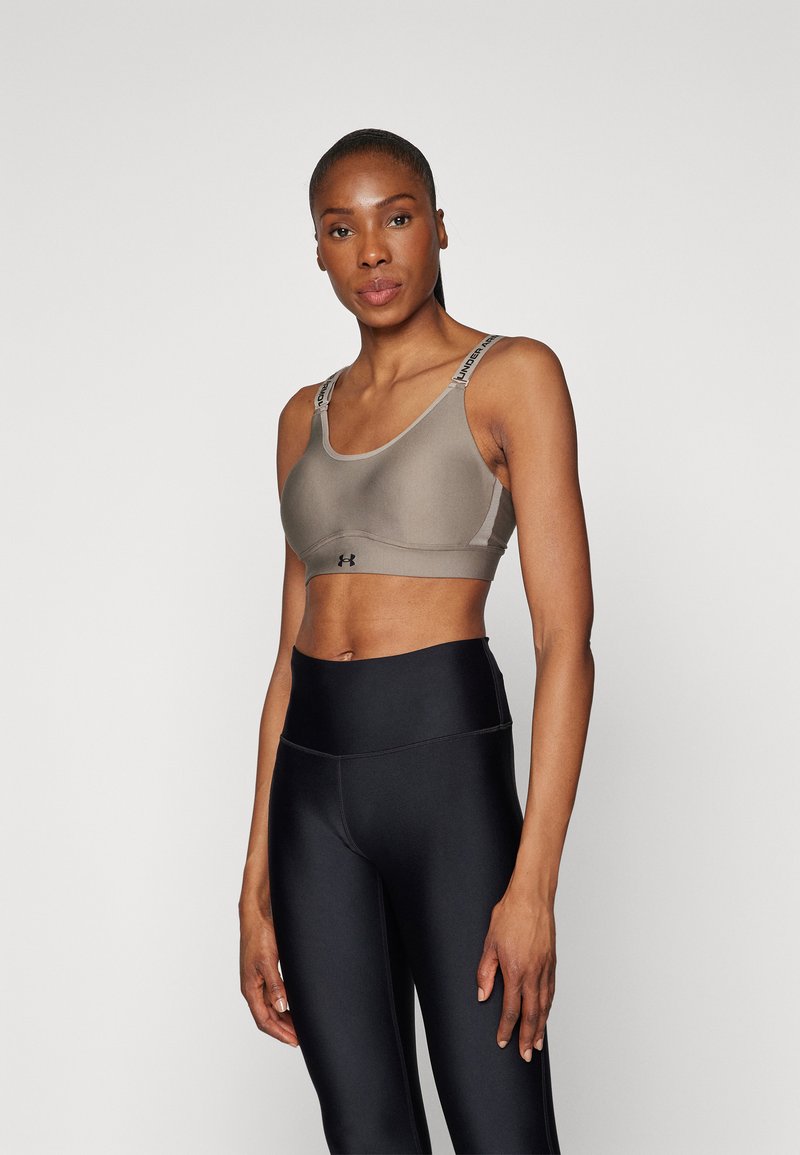 Under Armour sports-bh i taupe med grå detaljer, med justerbare stropper og et stilrent, stretchy design. Kombinert med svarte høyt liv leggings.