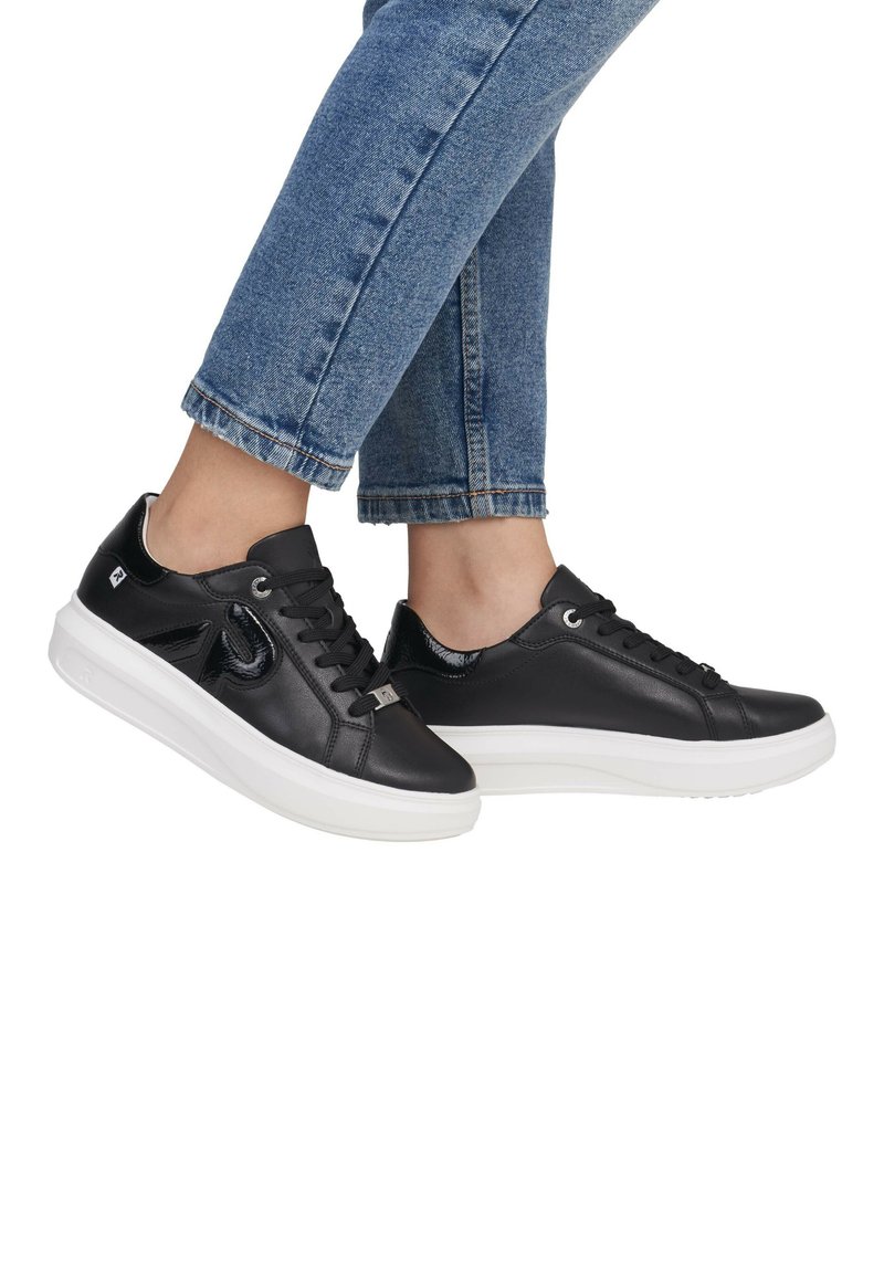 Baskets en cuir noir avec une finition lisse, semelle en caoutchouc blanche et bout arrondi. Dispose de lacets noirs et d'accents brillants. Pantalon en denim cropped visible.