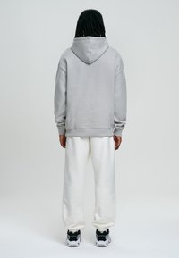 Sudadera con capucha de color gris claro con cordón, combinada con pantalones deportivos blancos y zapatillas negras. La tela parece suave y cómoda.