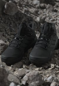 Stel zwarte hoge wandelschoenen met veters, geplaatst op rotsachtig terrein met losse stenen en ruwe grond.