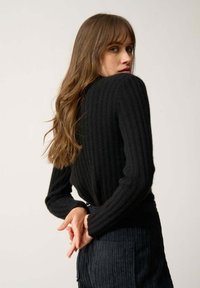 Czarny sweter prążkowany z długimi rękawami, teksturowana tkanina, dopasowany krój i detal z tyłu; w parze z teksturowanymi ciemnymi spodniami.