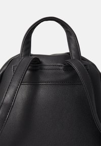Sac à dos en cuir noir avec surface texturée, deux bretelles et une poignée supérieure sur un fond uni.