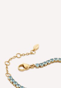 Bracciale dorato con gemme azzurro chiaro alternate e chiusura a gancio, con un piccolo tag goffrato che mostra il nome del marchio.