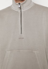 Felpa beige chiaro con zip al collo, colletto a coste, tasca frontale e logo 'BOSS' discreto. Realizzata in morbido tessuto testurizzato.