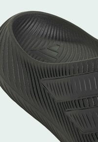 Primo piano di un sandalo ciabatta nero con tre strisce in rilievo e suola interna modellata per presa e comfort.