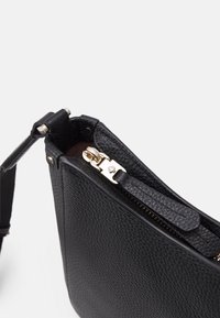 Sort lædertaske med en struktureret overflade, guldfarvet hardware lynlås lukning og en aftagelig rem. Har en indvendig lomme.