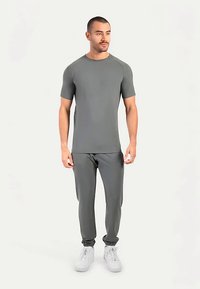 Grijze sportset van glad, rekbaar materiaal. T-shirt met korte mouwen en taps toelopende broek met elastische boorden. Gecombineerd met witte sneakers.