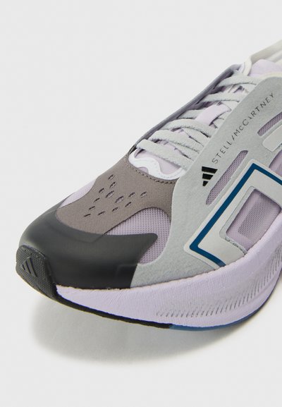 Running shoe in grey and lavender, featuring a black toe cap, mesh and suede panels, tonal laces, and a contrasting blue geometric detail.