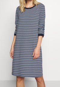 Robe tricotée rayée marine et blanche avec manches trois-quarts, col rond, et bordure unie marine au niveau de l'encolure et des poignets. Coupe régulière.