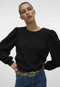 Sort ribbet langærmet top med puffede skuldre, parret med et beige og sort stribet bælte og blå denimshorts.