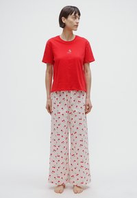 T-shirt en coton rouge avec un petit motif de bicyclette, associé à un pantalon clair, ample, orné d'un motif de cerises.