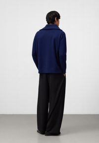 Maglione lavorato a maglia blu navy con un ampio colletto e maniche lunghe, abbinato a pantaloni neri a gamba larga. Design semplice e pulito, senza motivi.