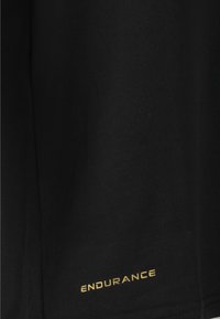 Svart tr�äningsskjorta i slät tyg, med en guldig "ENDURANCE"-logotyp nära fållen, med en enkel design och utan ytterligare mönster.