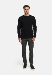 Svart strikket genser med rund hals, paired med grå teksturerte bukser og mørke joggesko. Passformen er slank og uformell.