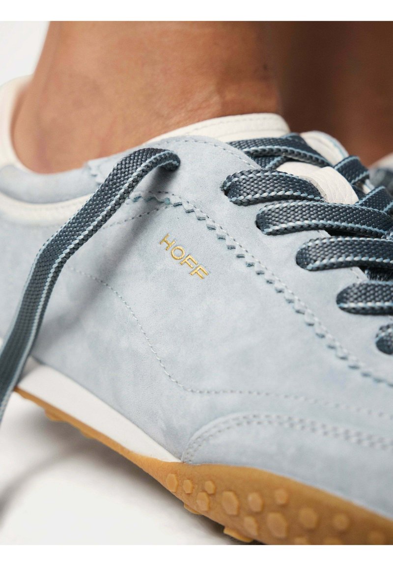 Baskets en daim bleu clair avec lacets bleu marine et semelle en caoutchouc beige, avec le nom de la marque "HOFF" en lettres dorées sur le côté.