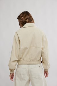 Hellbeige, kurze Jacke mit Kragen, elastischem Bund und gekrempelten Ärmeln, kombiniert mit hoch taillierten, off-white Hosen mit Taschen-Details.