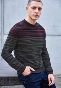 Pull à rayures foncées présentant des lignes horizontales dans des teintes de bordeaux, de vert et de noir. Fabriqué en tricot texturé, avec des poignets côtelés.