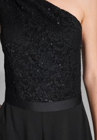 Schwarzes Spitzenkleid mit asymmetrischem Design, aufwendigen Blumenmustern, Pailletten und einem satinierten Taillenbund mit glatter Stoffoberfläche.