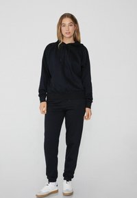 Schwarzer Baumwoll-Hoodie mit verstellbarem Kordelzug, gerippten Bündchen und passenden schwarzen Jogginghosen, die eine lockere Passform und Knöchel-Bündchen aufweisen.