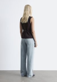 Schwarzes ärmelloses Oberteil mit einem Schnallen-Detail auf der Rückseite, kombiniert mit hellblauen weiten Jeans. Glatte Stoffe, minimalistisches Design.