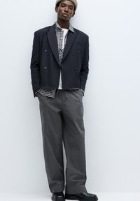 Sort dobbeltradet blazer med nålestriber over en ternet skjorte med grå bukser, kombineret med sorte støvler. Glatte teksturer og skræddersyet pasform.