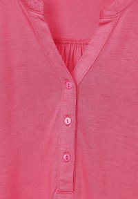 Camisetta rosa a V in tessuto liscio, con cinque bottoni abbinati lungo la pattina e dettagli arricciati al colletto.