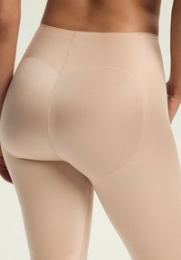 Beżowe legginsy bezszwowe o gładkiej fakturze, z wysokim stanem oraz konturowymi akcentami na plecach dla wsparcia i poprawy kształtu.