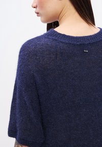 Πλεκτό πουλόβερ σε ναυτικό μπλε χρώμα με υφή και κοντά μανίκια, διαθέτοντας �μια διακριτική ετικέτα στο πίσω μέρος κοντά στη λαιμόκοψη.