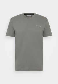 Šedé bavlněné tričko s krajkovým výstřihem a krátkým rukávem. Na levé straně hrudi je decentní bílé logo "Calvin Klein". Hladká textura.